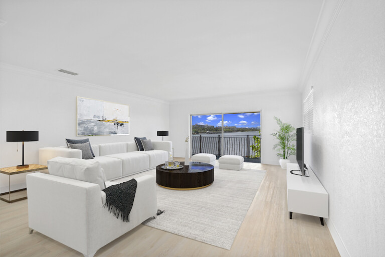 Bright, modern living room with white sectional seating, a round dark wood coffee table, and large sliding glass doors leading to a balcony facing the Intracoastal Waterway.