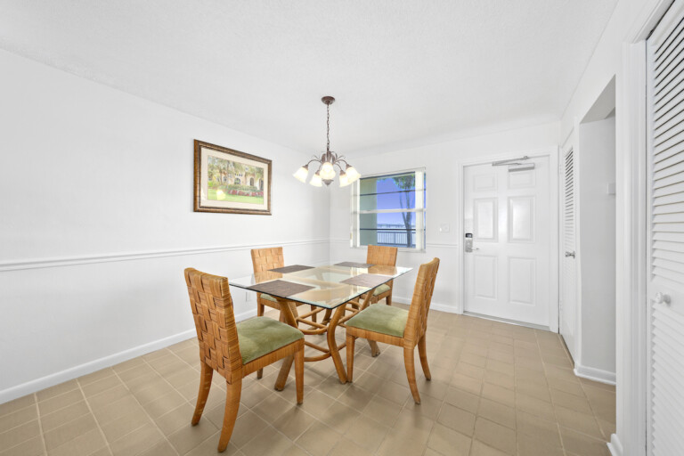Bright dining room with a glass-top rattan table, woven chairs, a classic chandelier, window, and white entrance door.
