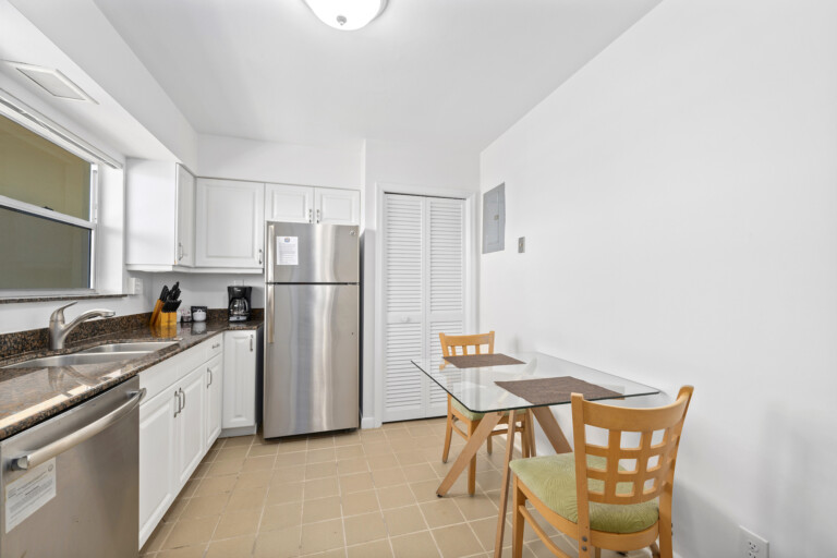 Kitchen and dining area featuring white cabinets, granite countertops, stainless steel appliances, and a glass-top table with wooden chairs.