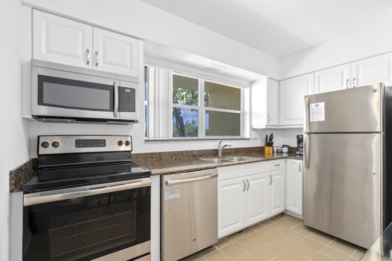 Kitchen featuring white raised-panel cabinetry, dark granite countertops, and stainless steel appliances with a window over the sink.